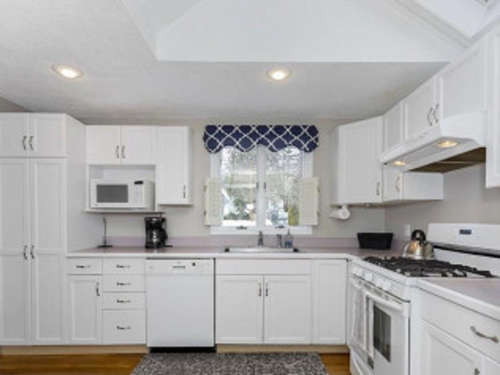 White kitchen with white cabinets, appliances, and a window with a blue and white valance.