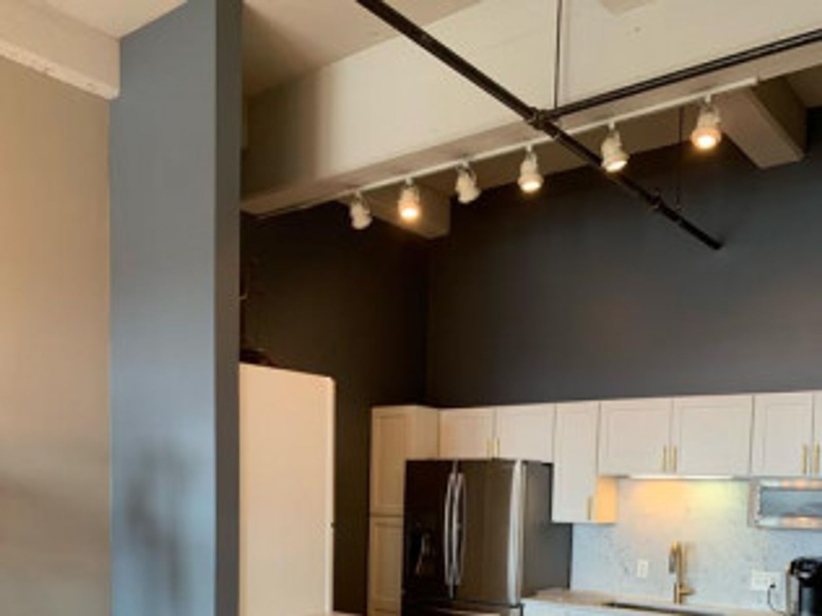 Modern kitchen interior with white cabinets, stainless steel refrigerator, and track lighting.