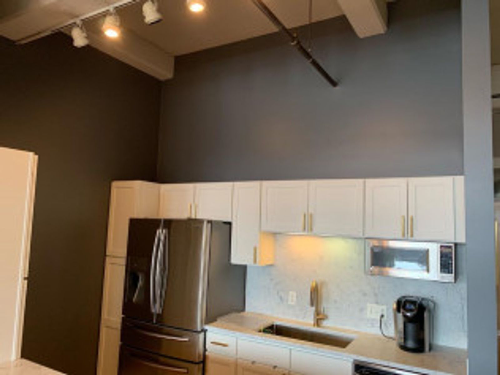 Modern kitchen with white cabinets, stainless steel appliances, dark gray wall.