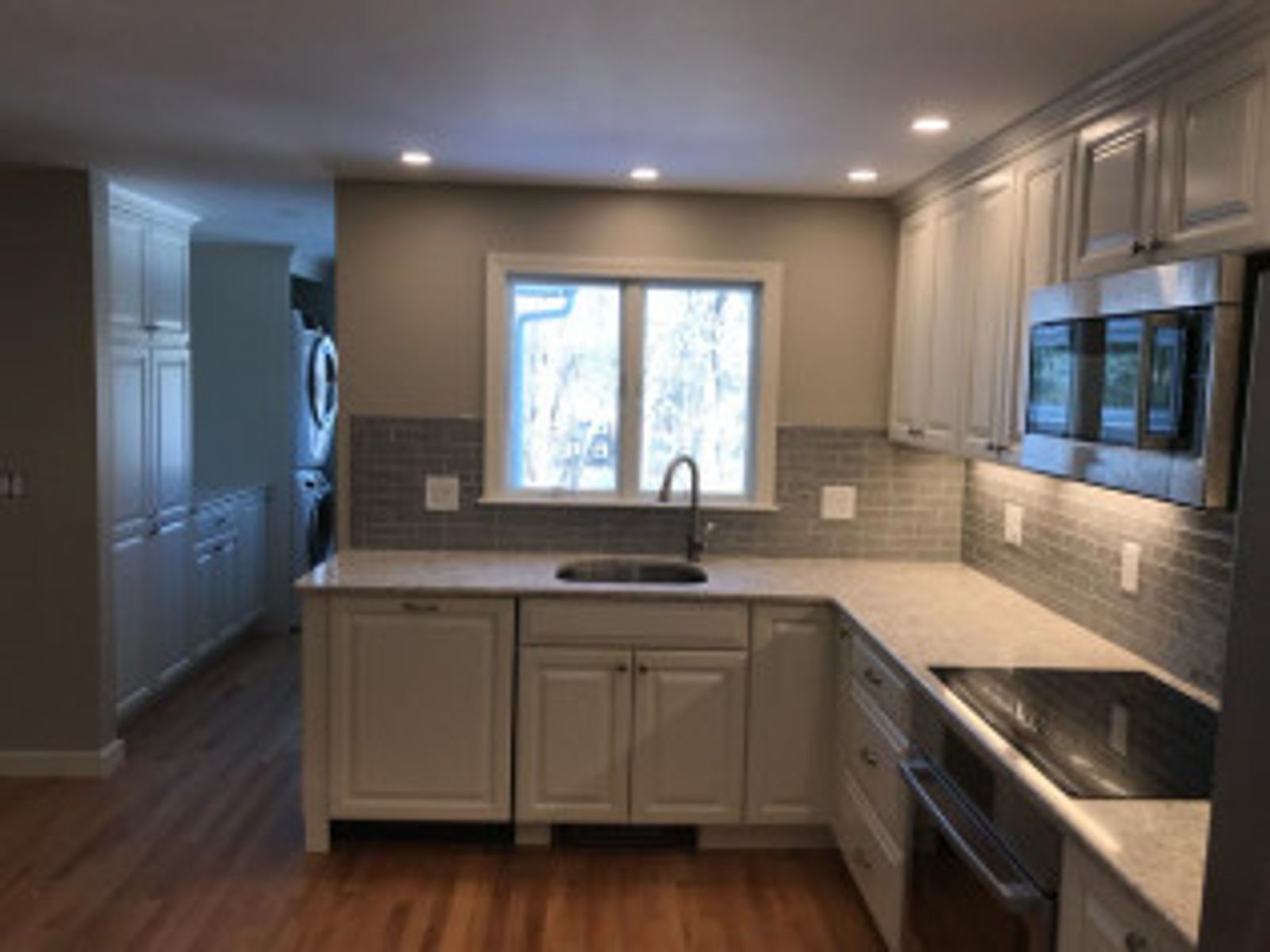 Modern kitchen with white cabinets, gray backsplash, and stainless steel appliances.