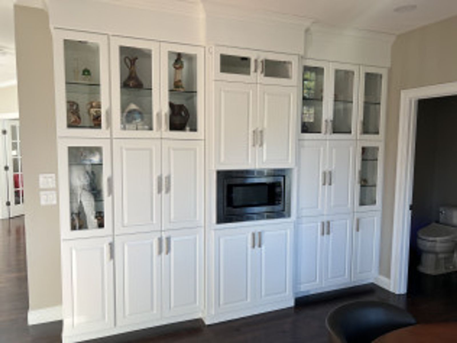 White kitchen cabinets with glass doors, microwave, and hardware against tan walls.