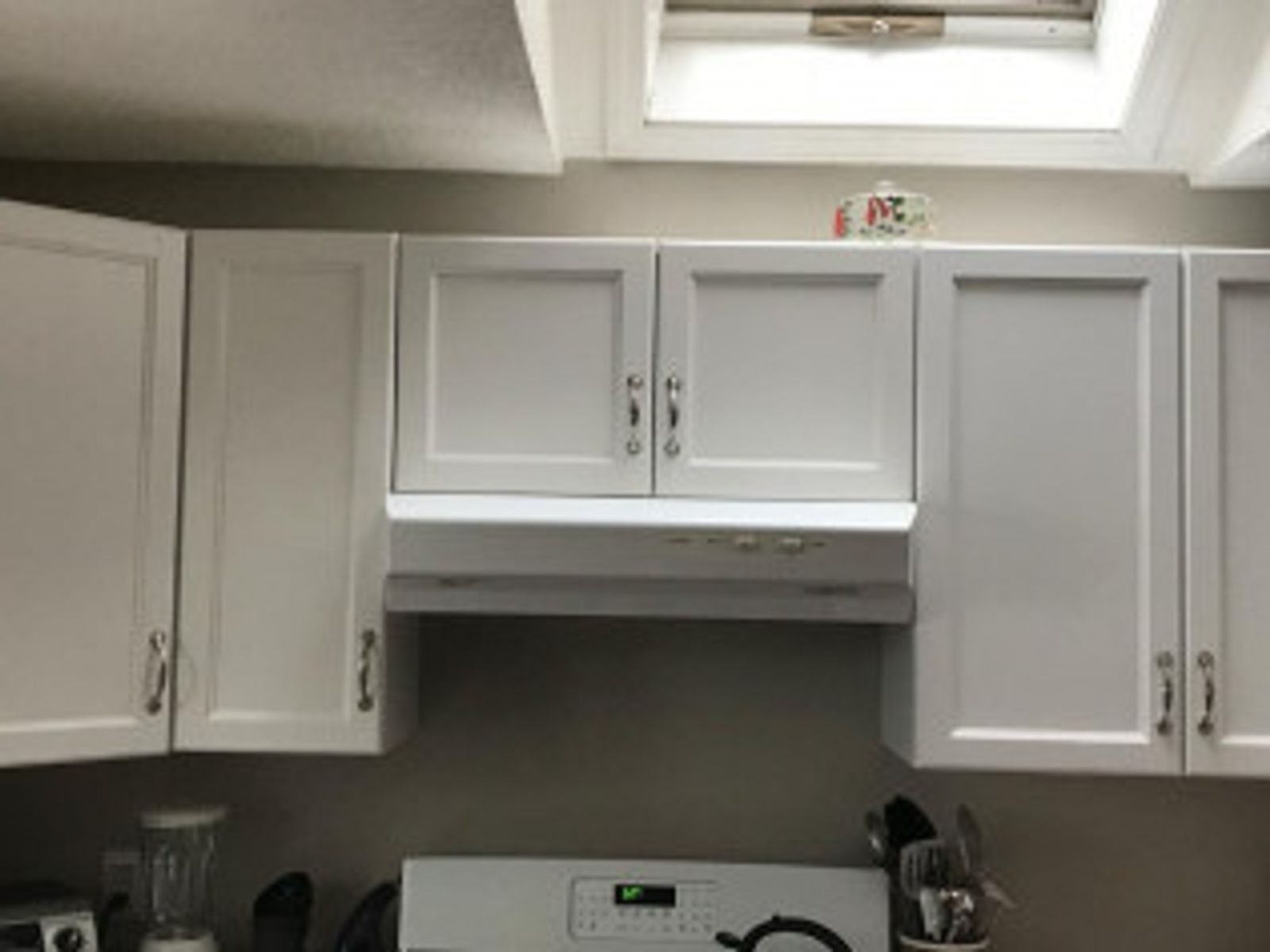 White kitchen cabinets above a stove, with a range hood and a skylight.