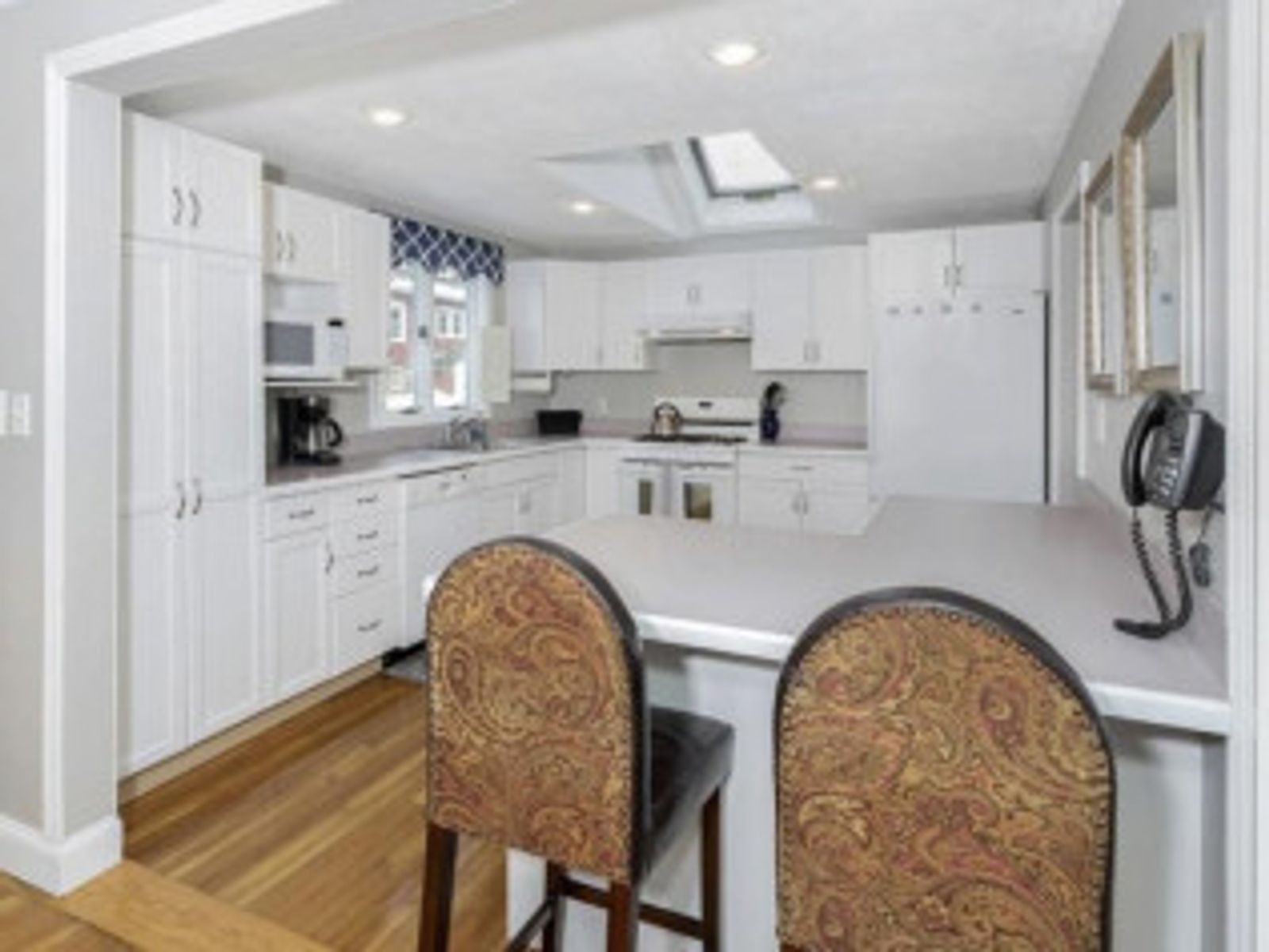 White kitchen with bar seating; wood floors, white cabinets, and a skylight.