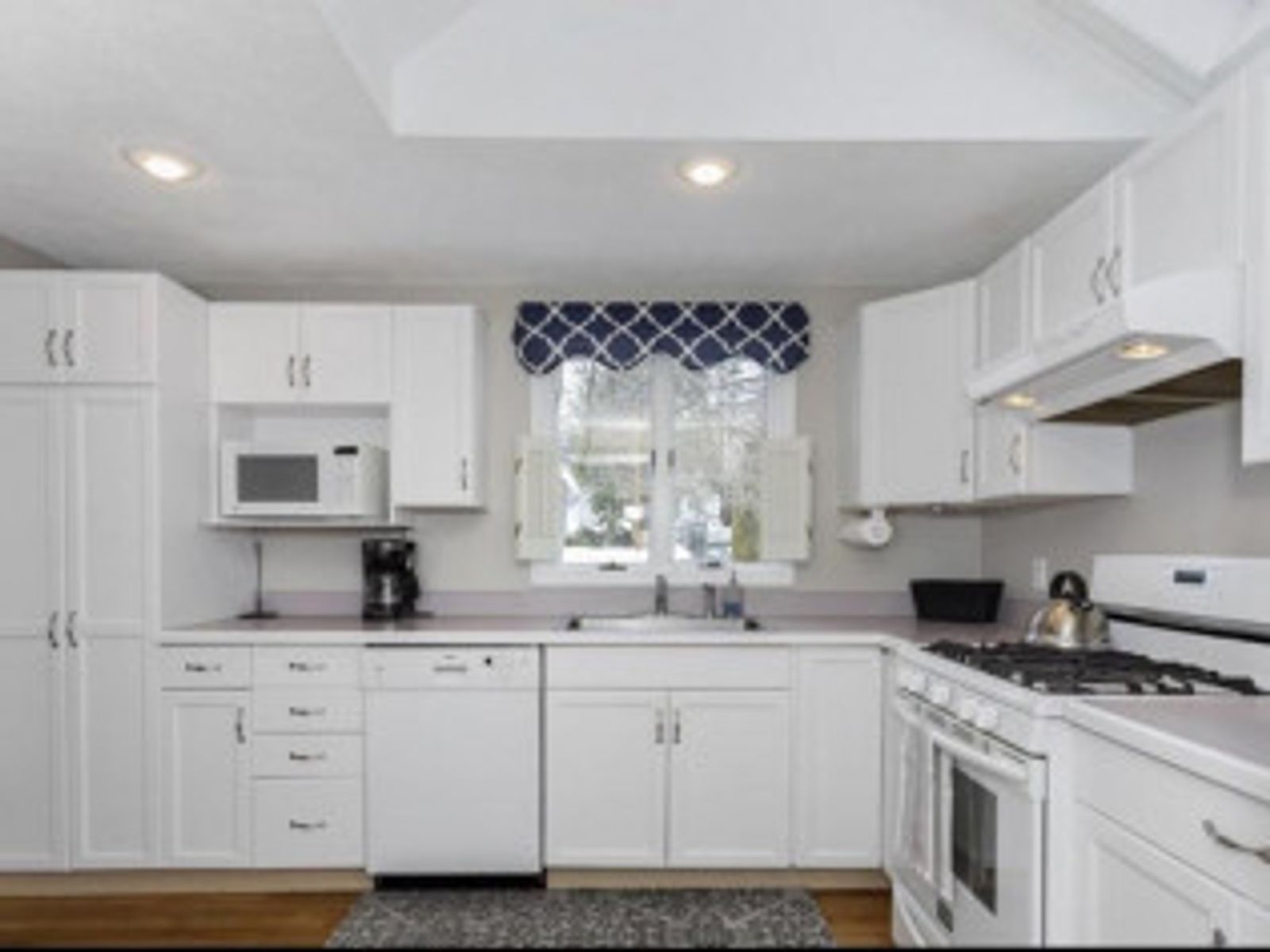 White kitchen with white cabinets, appliances, and a blue and white patterned window valance.