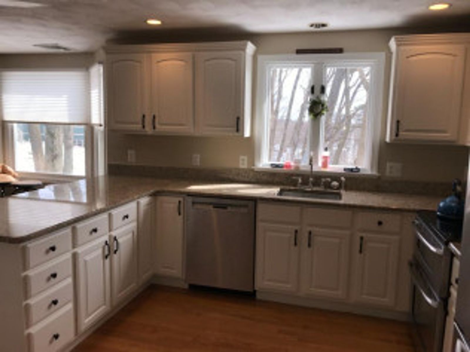 White kitchen cabinets with black hardware, stainless steel appliances, and beige countertops.