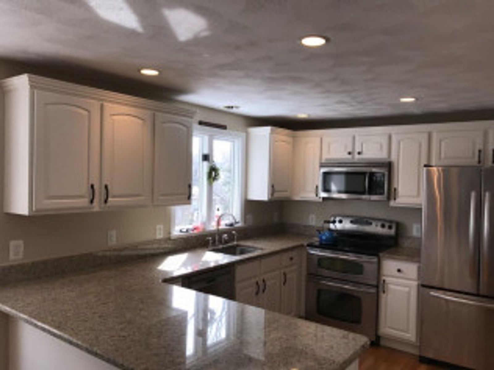 White kitchen cabinets with granite countertops, stainless steel appliances, and a window above the sink.