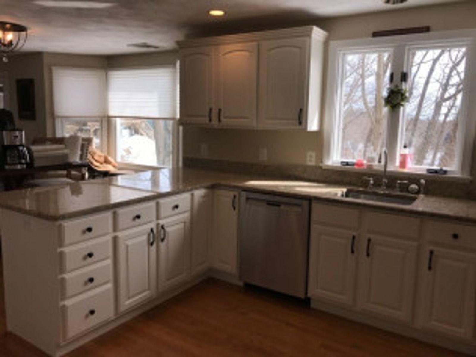 White kitchen with granite countertops, stainless steel dishwasher, and a window with a snowy view.