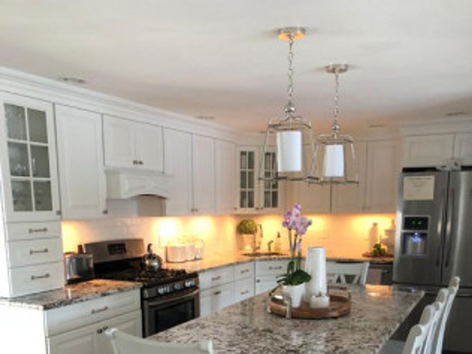 White kitchen with granite countertops, stainless steel appliances, and two hanging lanterns.