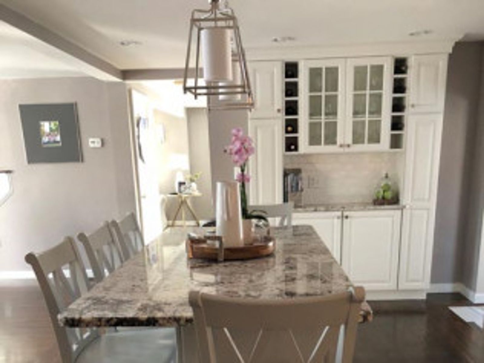 Dining room with marble-topped table, white cabinets, and chairs. A hanging light fixture and orchid are present.