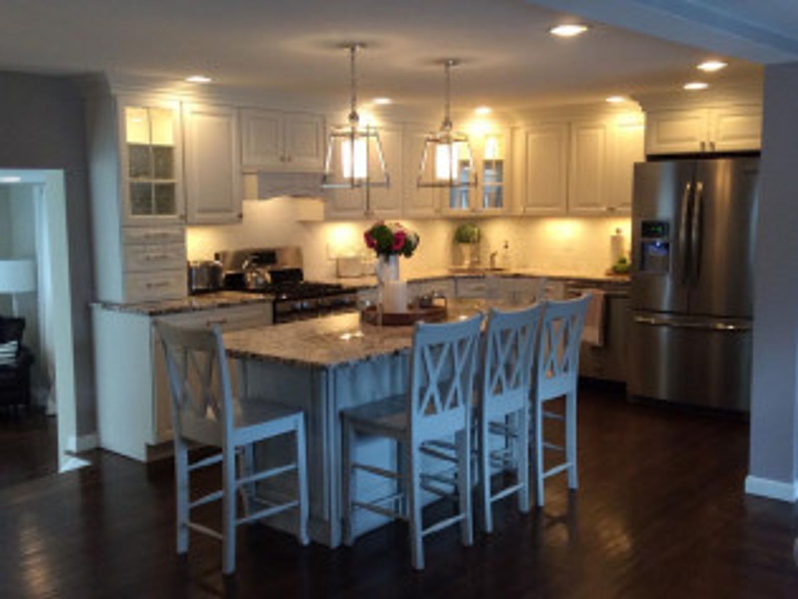 Bright kitchen with island seating, pendant lights, stainless steel appliances, and dark wood floors.