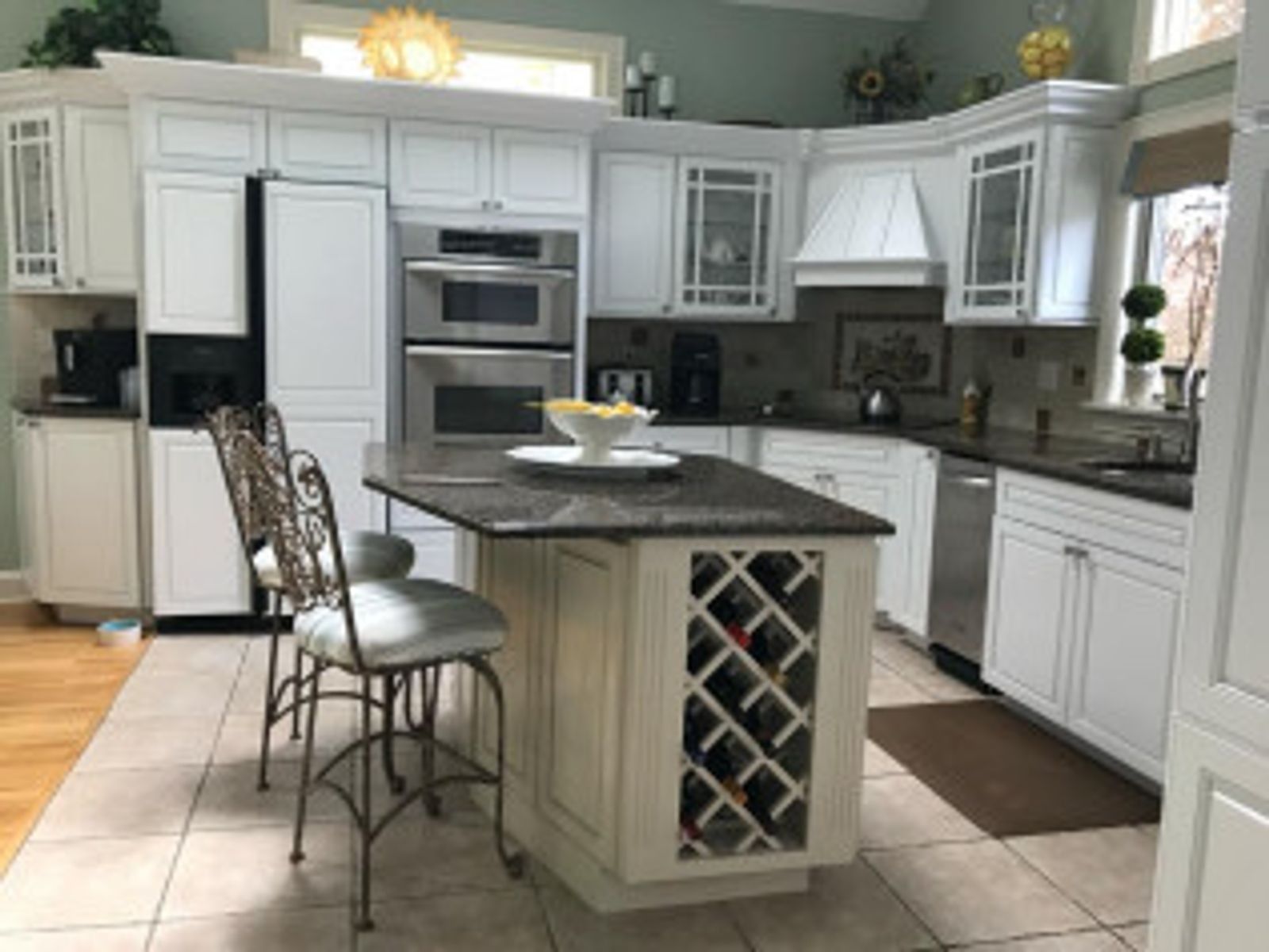 White kitchen with island, built-in appliances, and tile floor; two ornate bar stools.