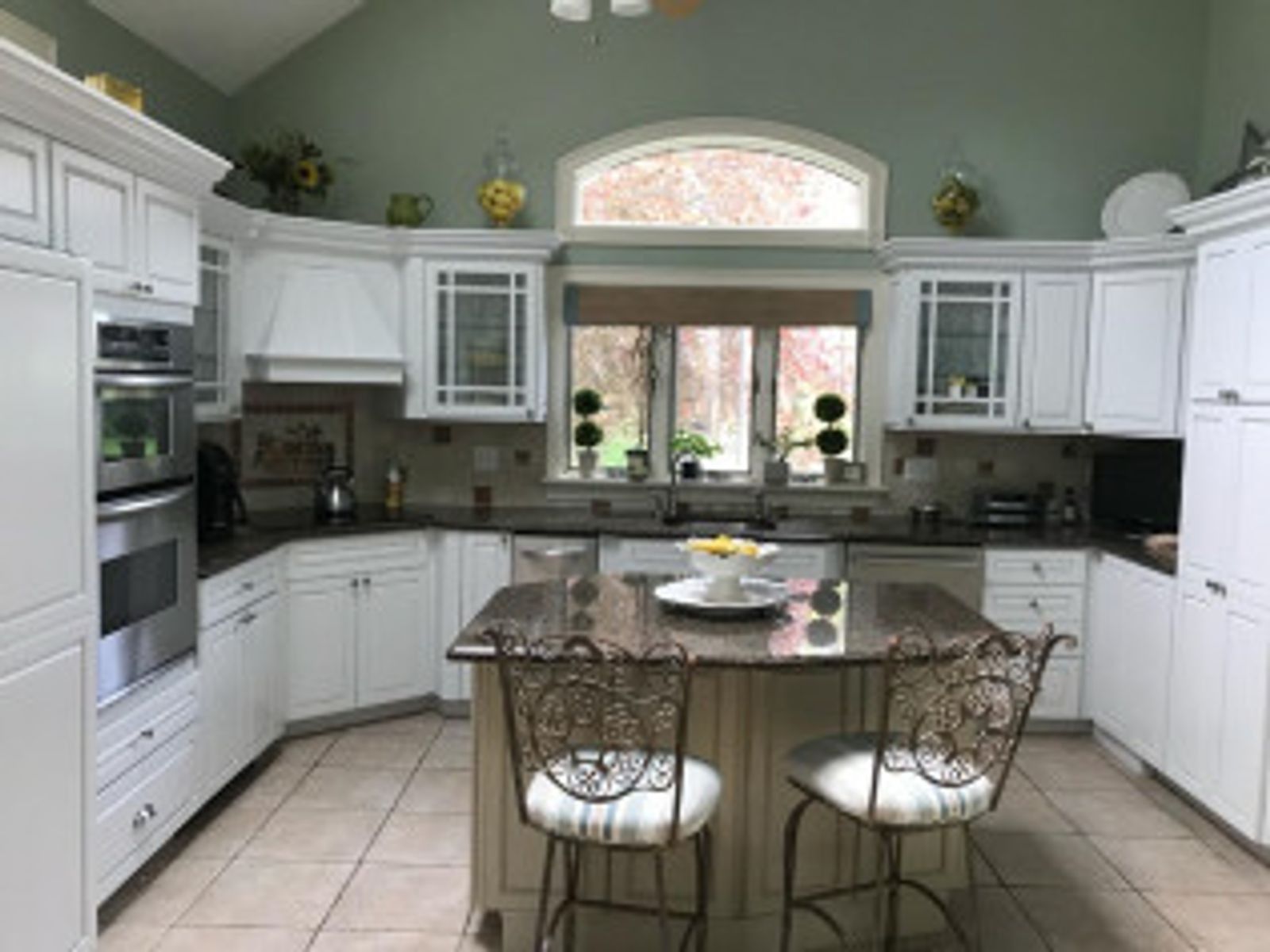 White kitchen with granite countertops, island with chairs, and arched window.