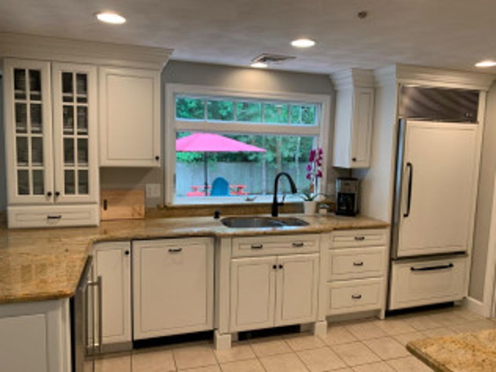 White kitchen with granite countertops, stainless steel appliances, and a window overlooking a backyard.