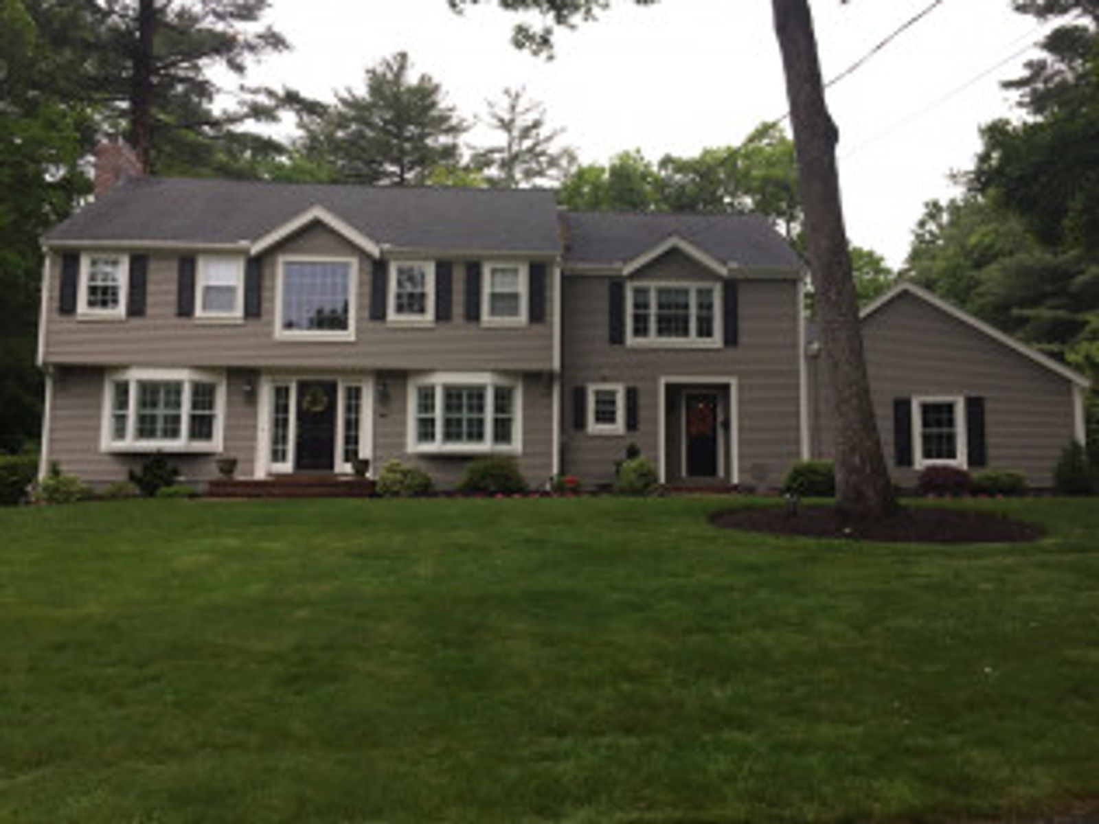 Two-story gray house with black shutters, bay windows, and a green lawn.