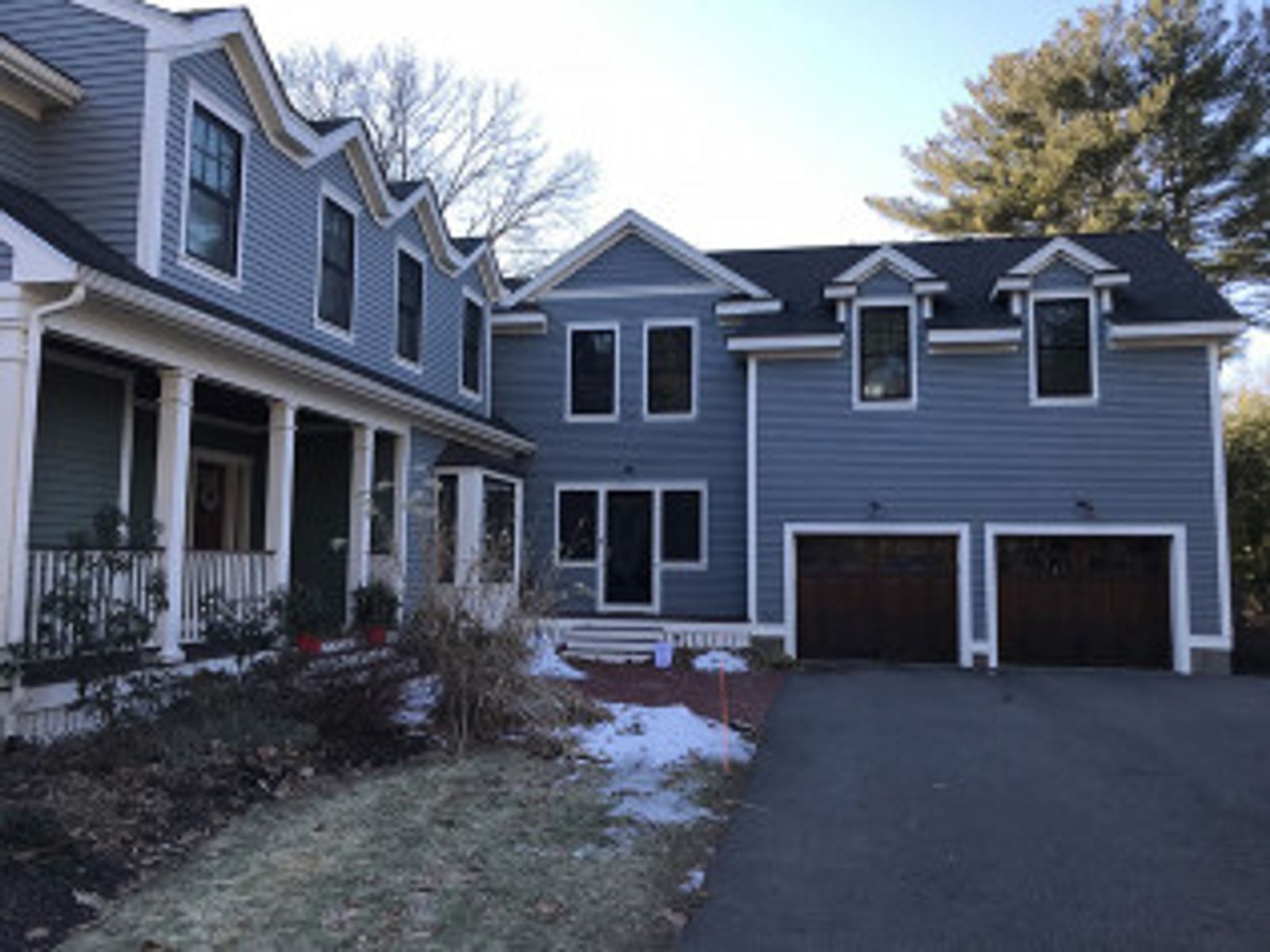 Blue-sided house with a porch and two-car garage; brick walkway with patches of snow; sunny day.
