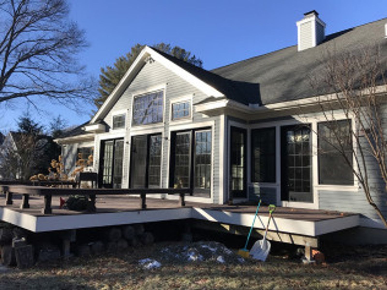 Deck and house exterior on a sunny day. Gray siding, black doors and windows, and a dark deck.