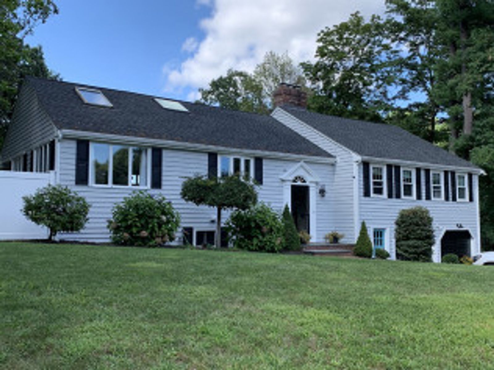 Light blue house with dark shutters, black roof, and green lawn.