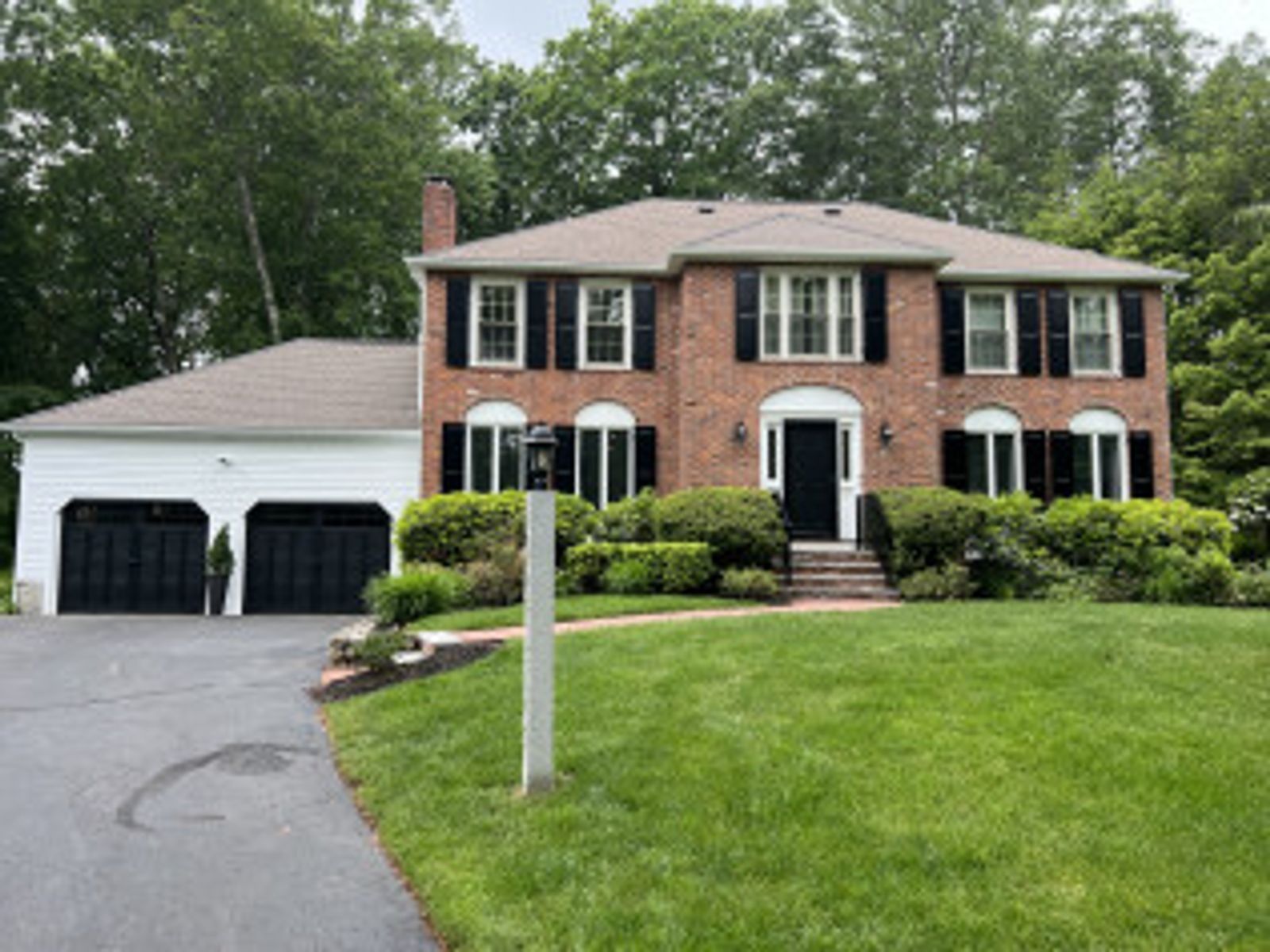 Two-story brick house with black shutters, a two-car garage, and green lawn.
