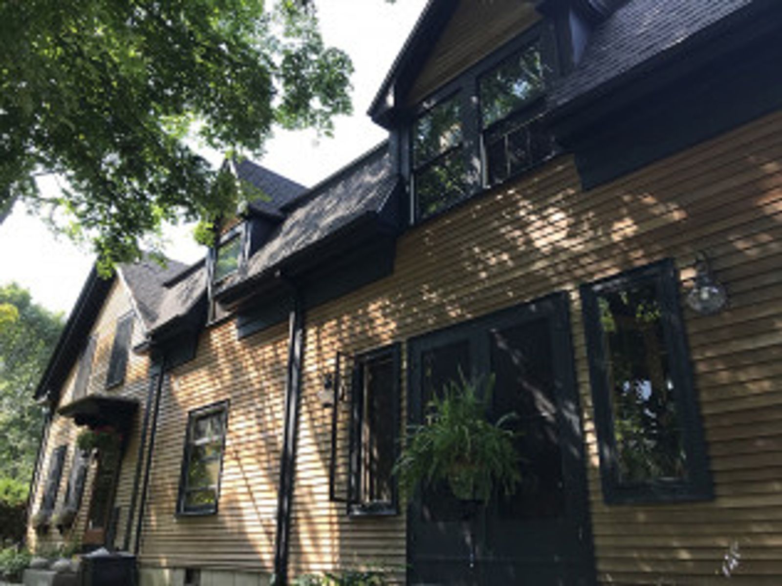 Two-story house with wooden siding, black trim and windows, and a shaded exterior.