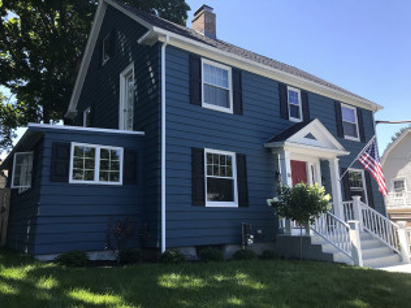 Blue house with white trim, black shutters, and red door. American flag displayed on the right.