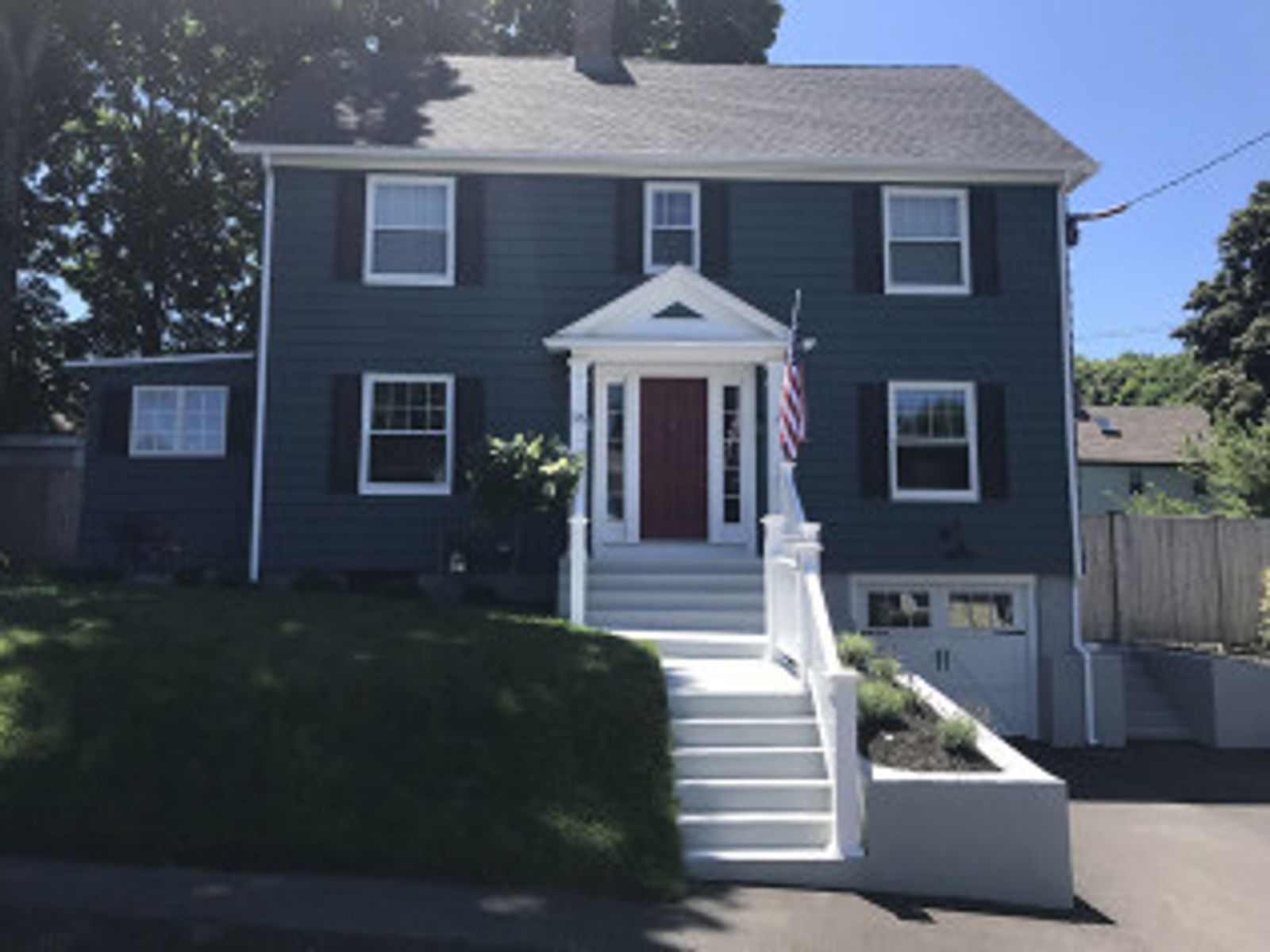 Blue two-story house with white trim, red door, American flag, and white steps leading to the entrance.