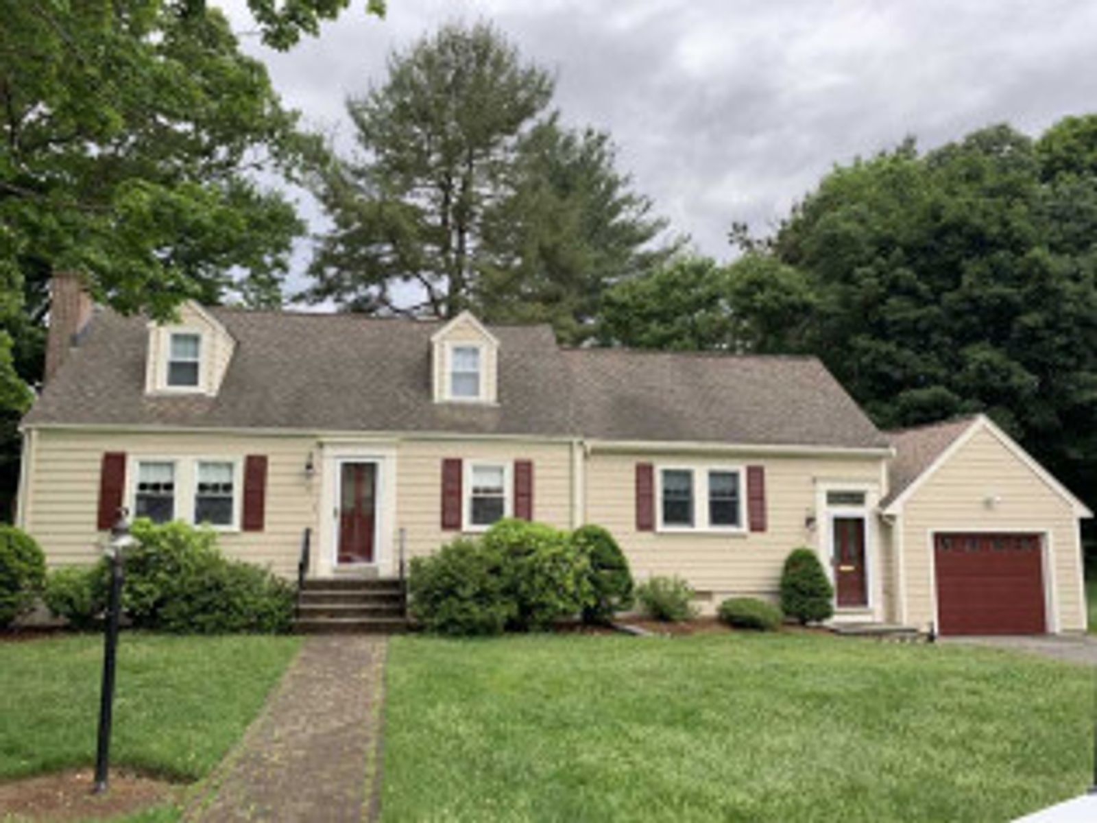 Tan house with brown shutters and garage, dormers, and a green lawn.