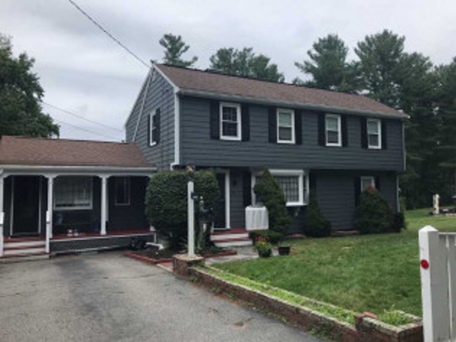 Two-story gray house with black shutters, porch, and a driveway on a cloudy day.