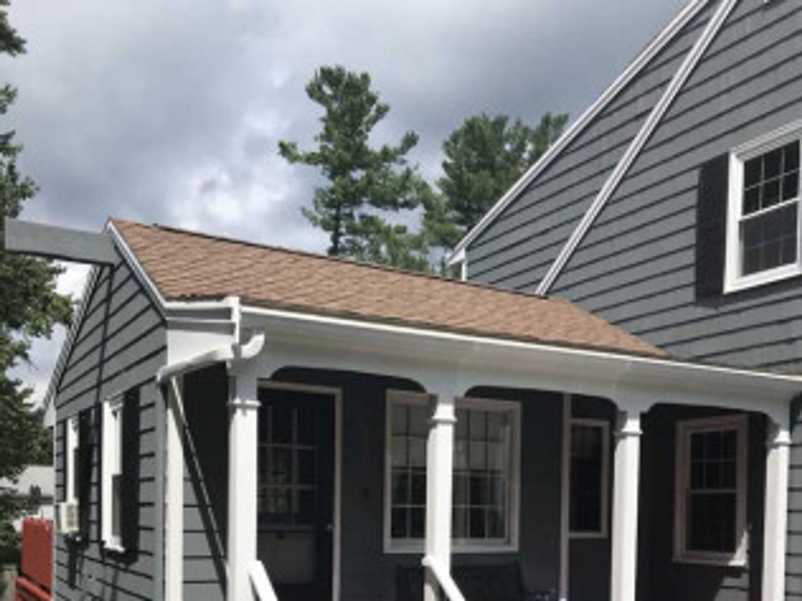 Gray house with white columns, windows, and brown roof. Cloudy sky.