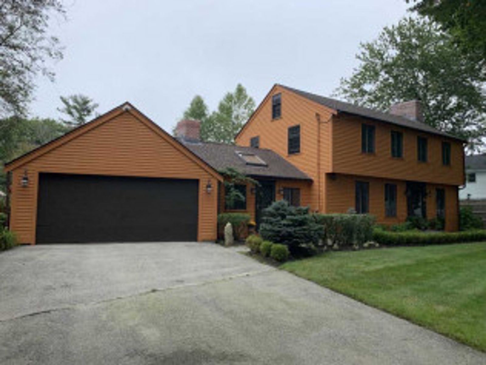 Two-story house with orange siding, attached garage, gray driveway, and green lawn.