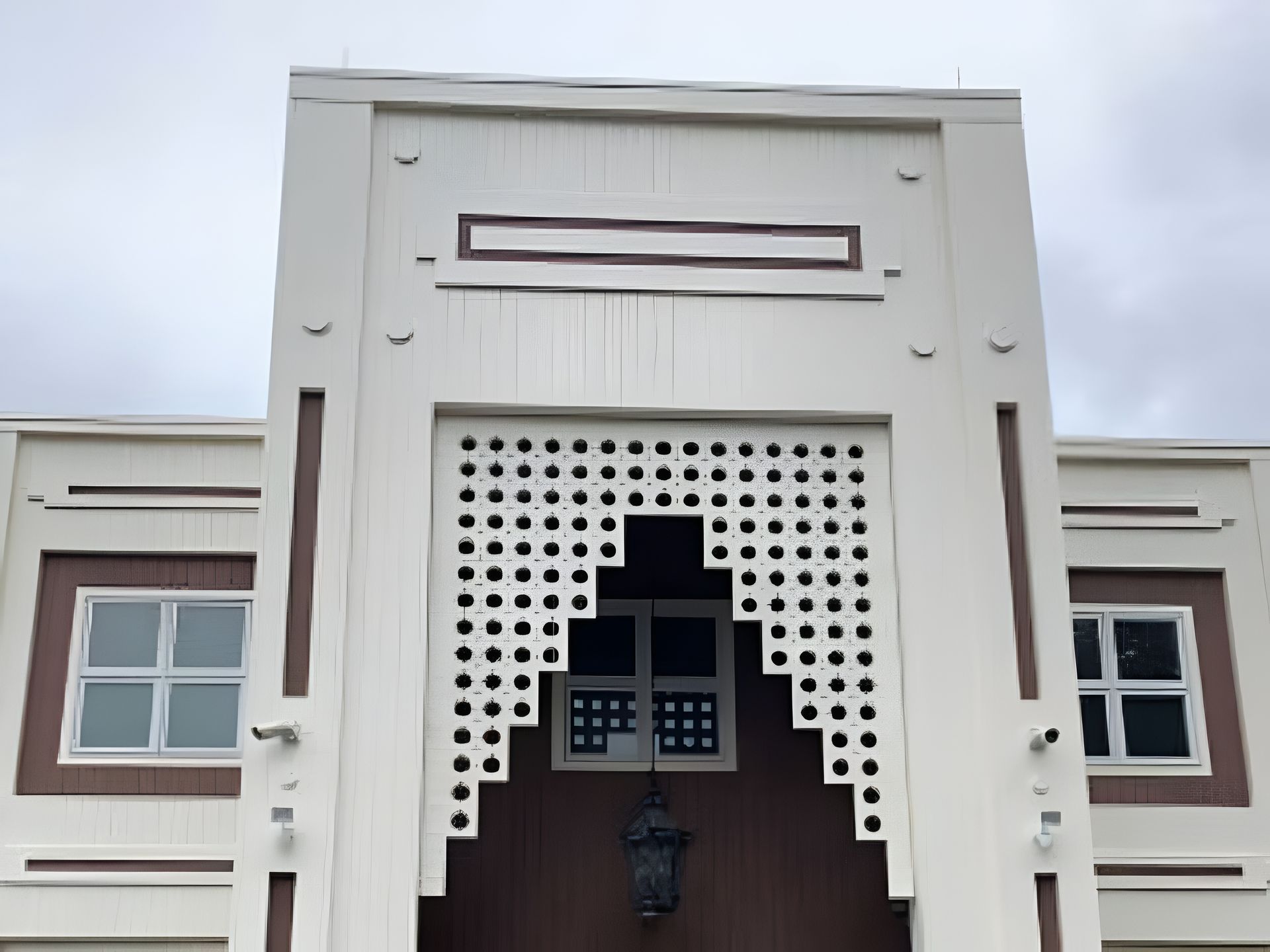White building facade with decorative cutouts and windows against a cloudy sky.