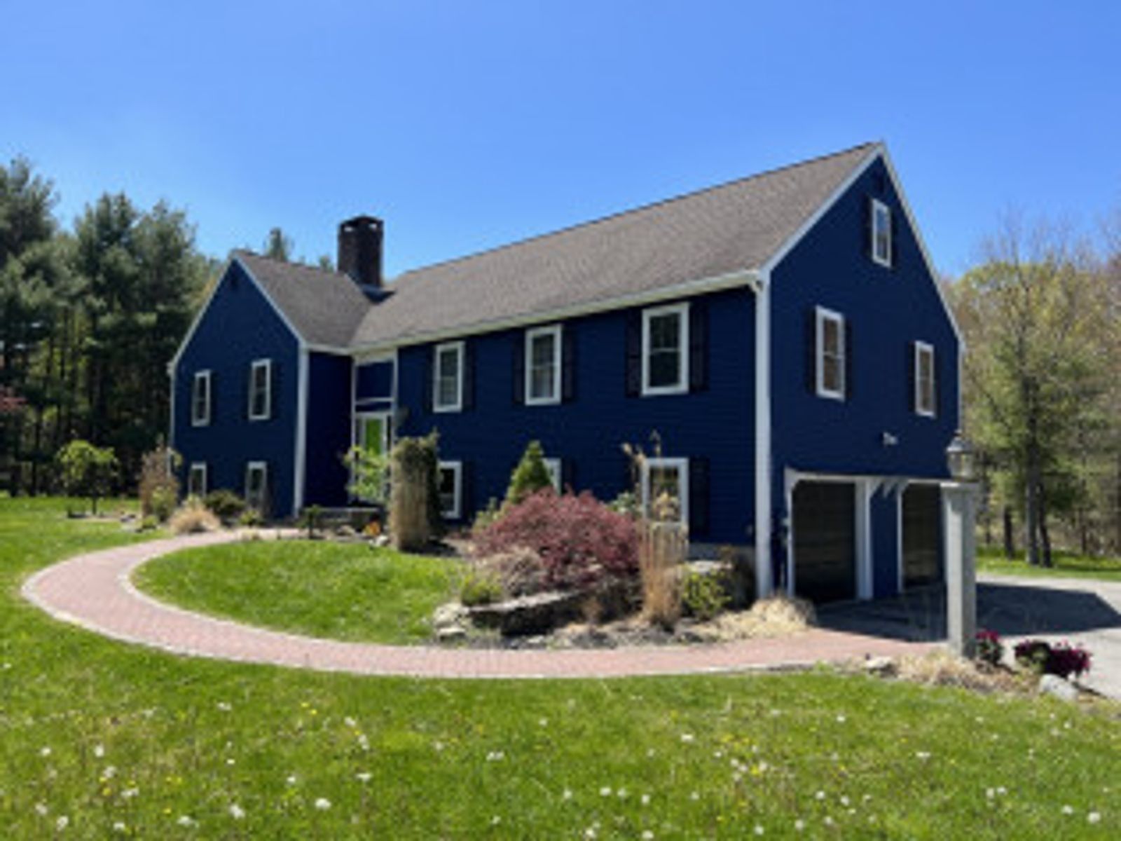 Blue house with white trim, black roof, and brick walkway on a sunny day.