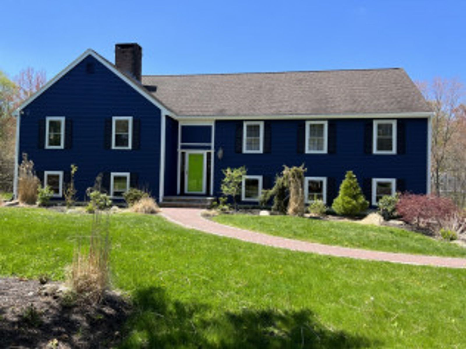 Blue house with green door, white trim, black shutters, brick pathway through green lawn.