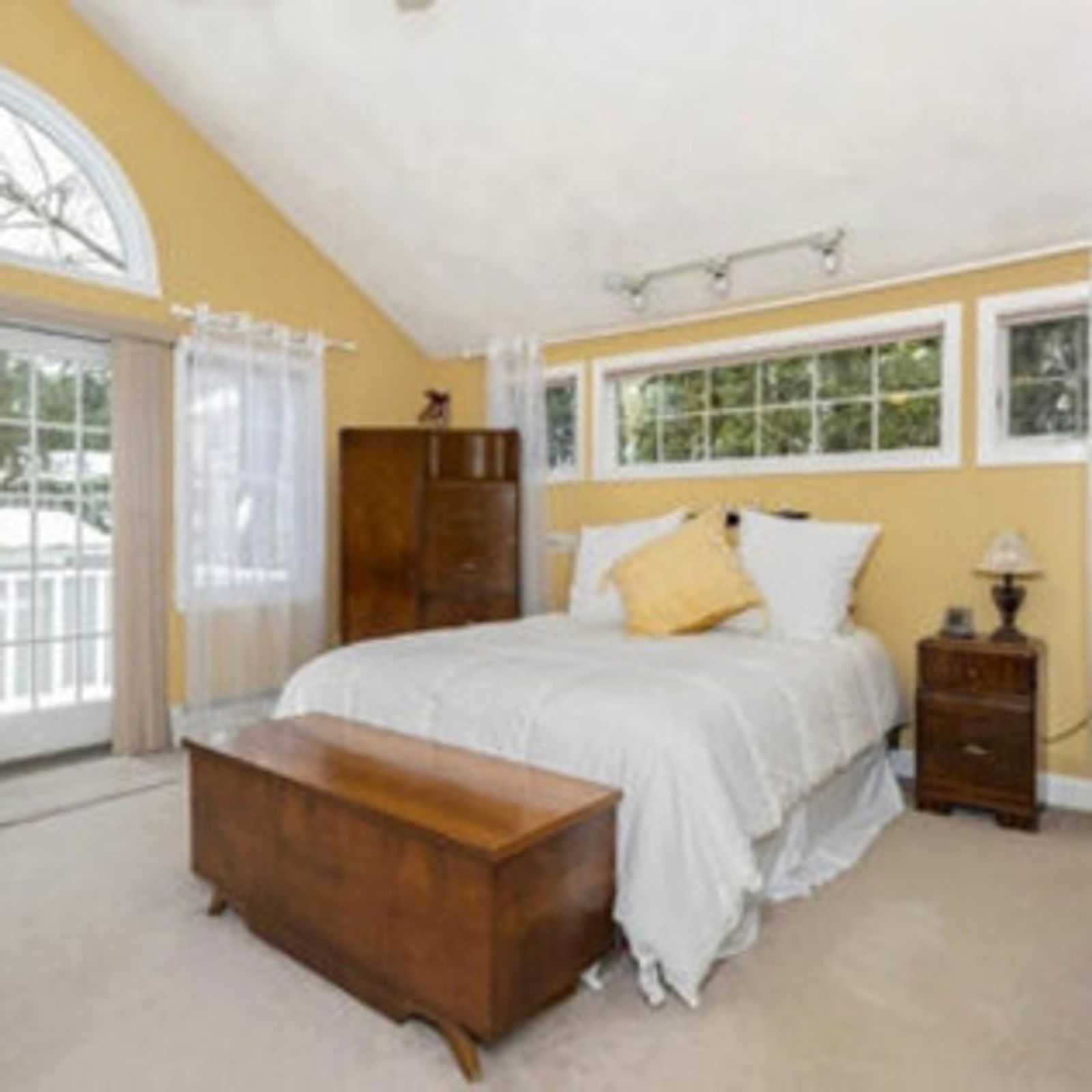 Bedroom with yellow walls, white bed, wooden furniture, and arched window.