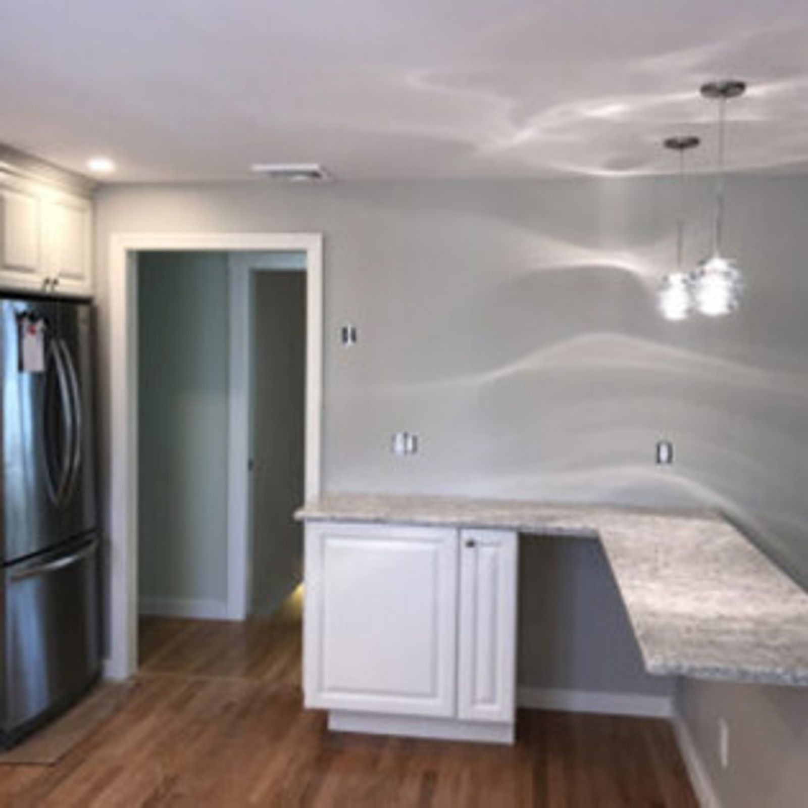 Kitchen with stainless steel refrigerator, white cabinets, granite countertop, and pendant lights.