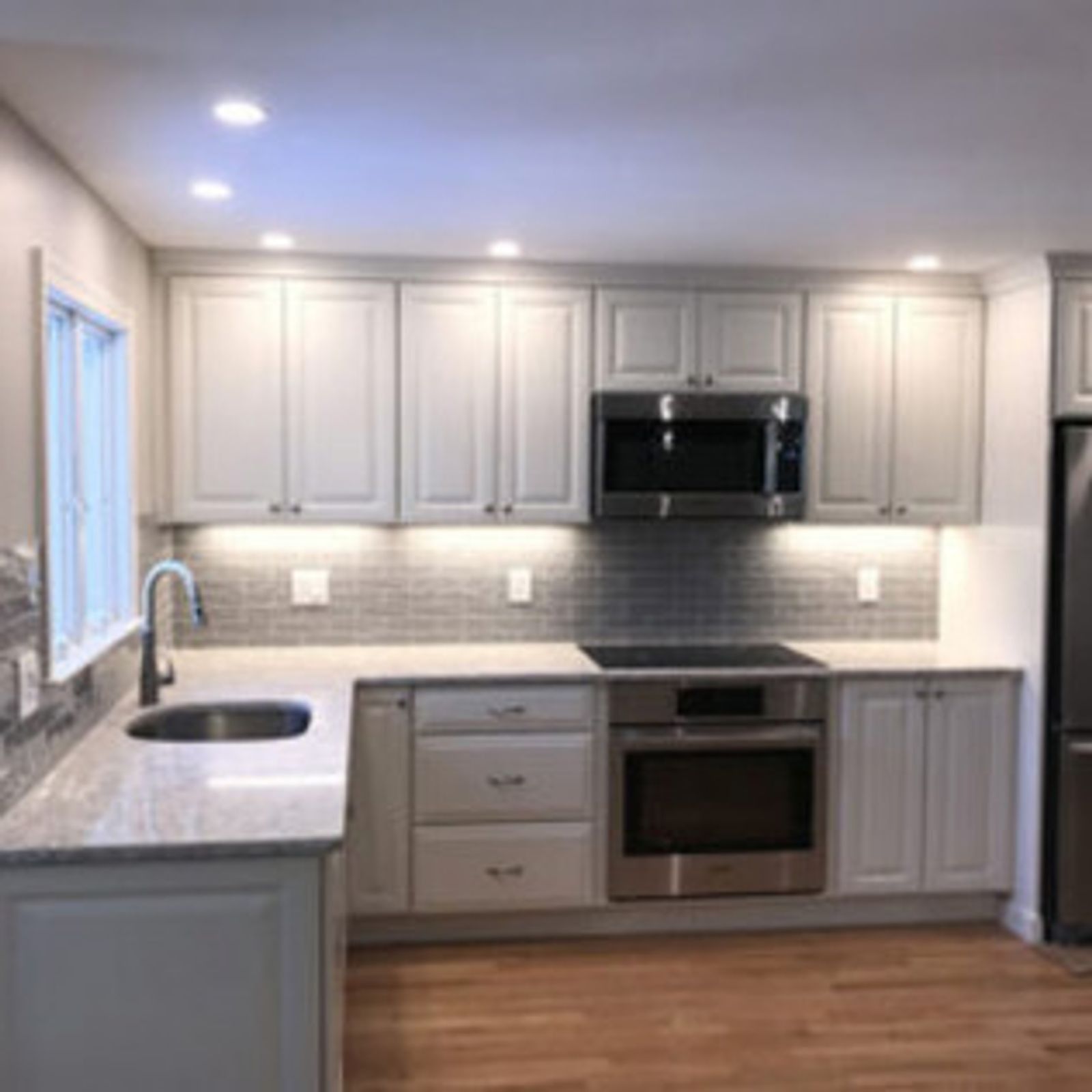 Gray kitchen with light-colored cabinets, stainless steel appliances, and a tiled backsplash.