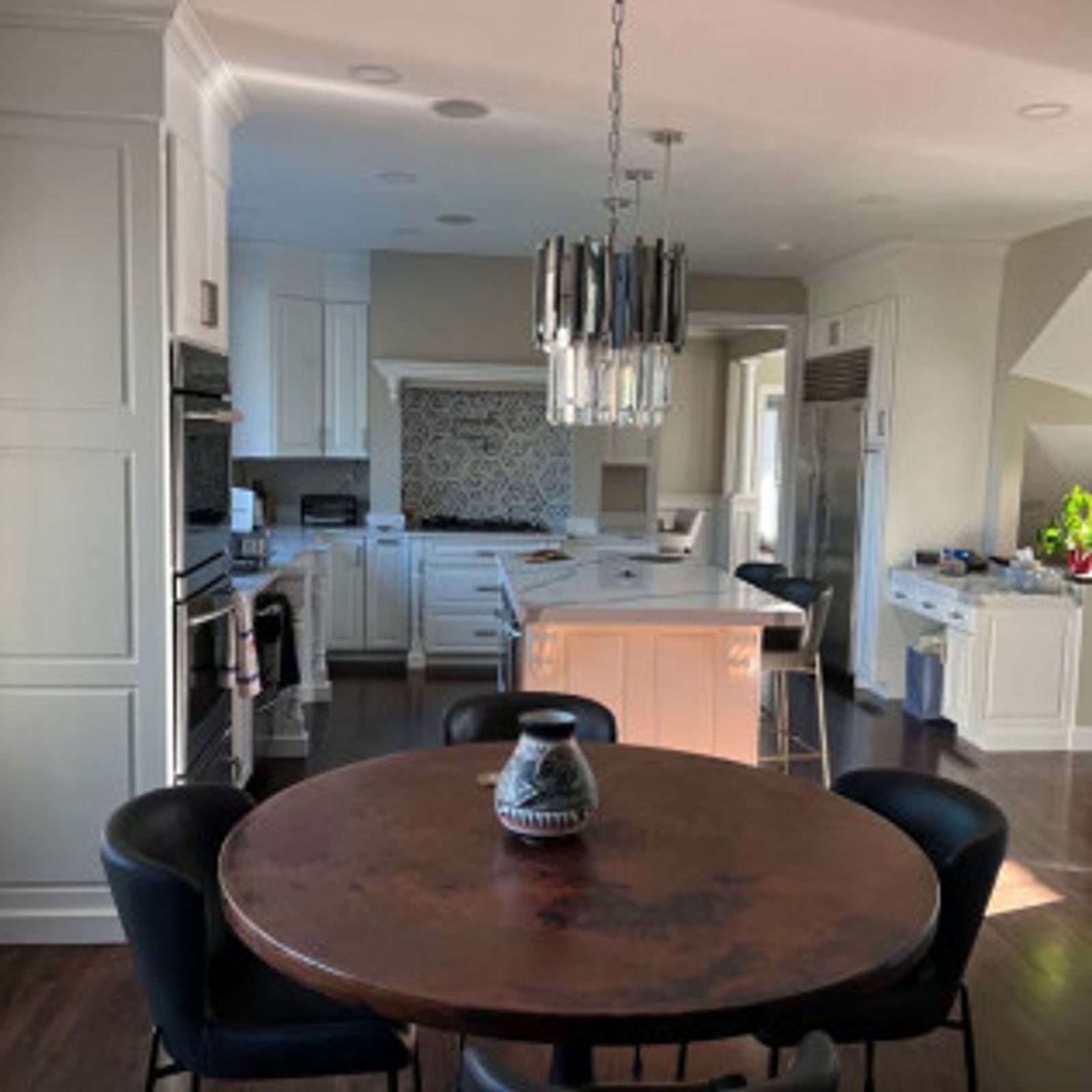 Kitchen with a copper-topped table and chairs; white cabinets and island; chandelier; and stainless steel appliances.
