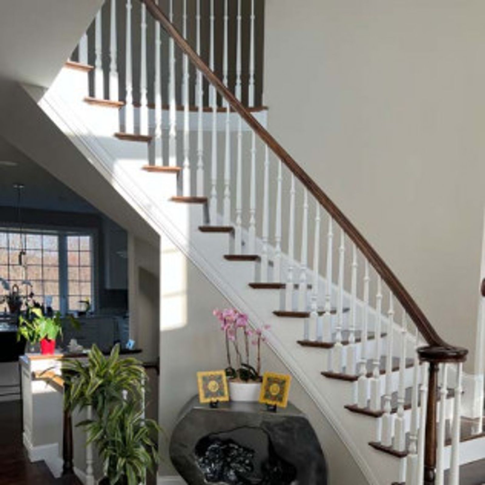 Staircase with white spindles, brown steps and handrail, and a curved bottom. Light streams in.