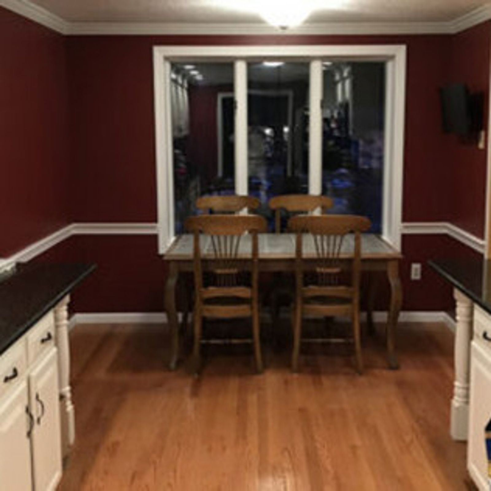 Kitchen with red walls, white trim, wooden floor, table with four chairs by a window.