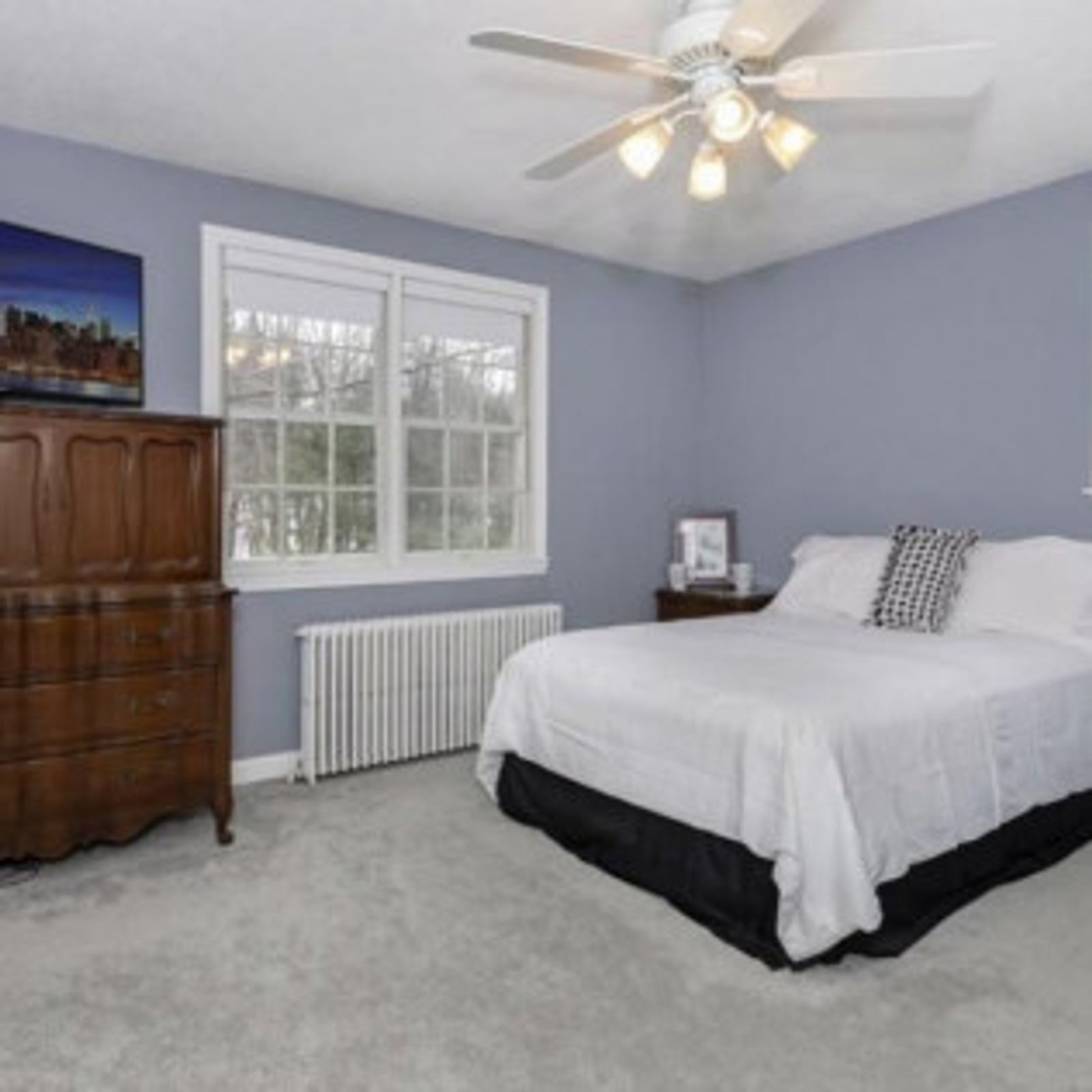 Bedroom with blue walls, white bedding, wooden dresser, and a window.