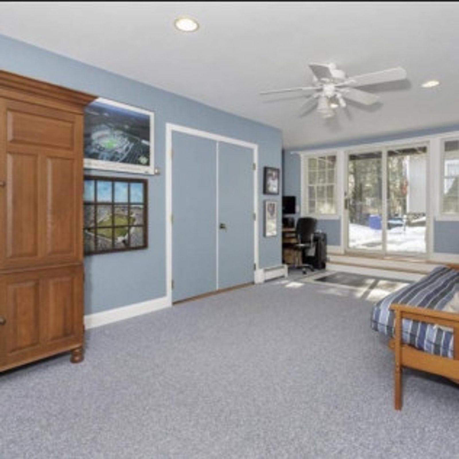 Bedroom with blue walls, closet, wooden armoire, and sliding glass doors.