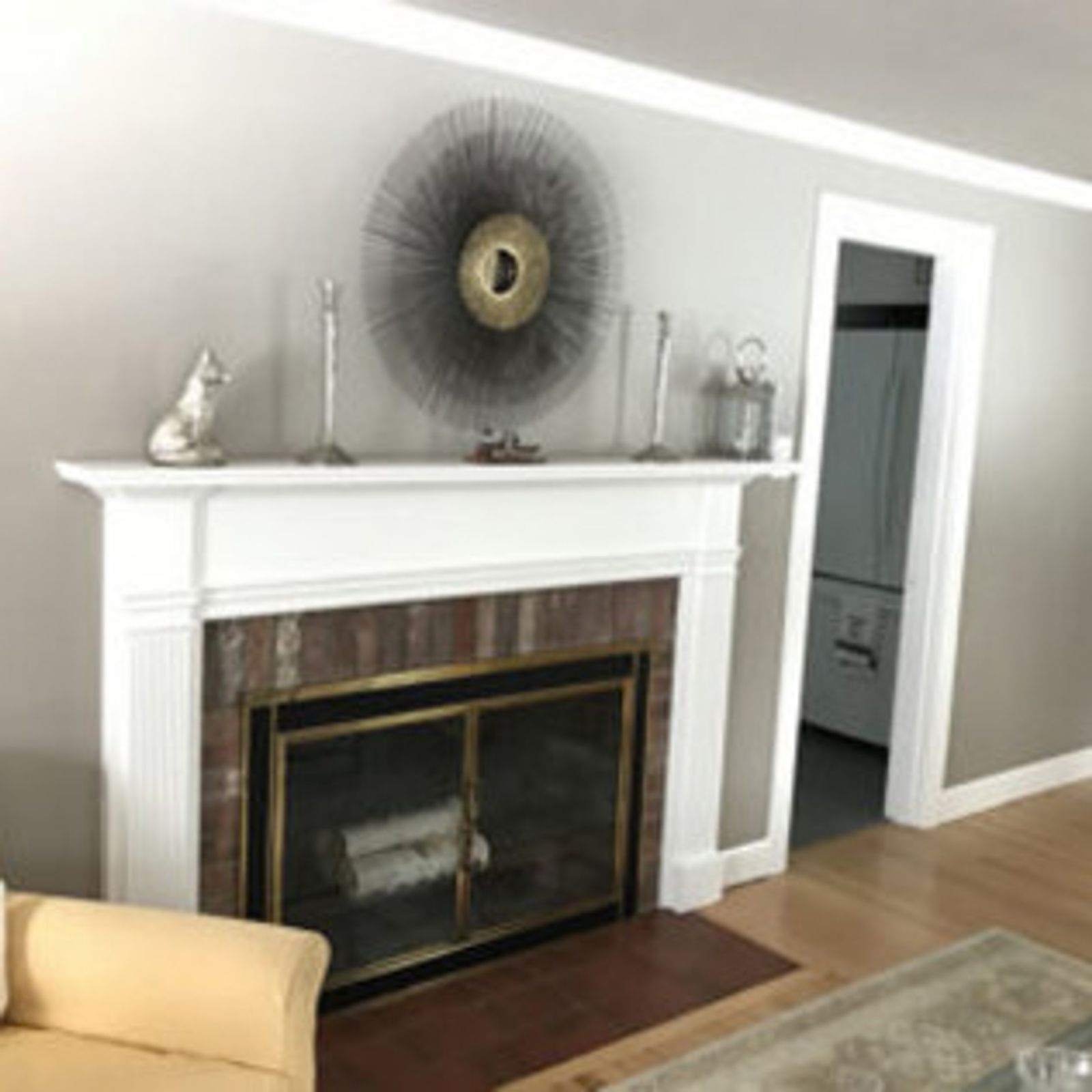 Fireplace with white mantel, brick surround, and decorative metal art on a gray wall.