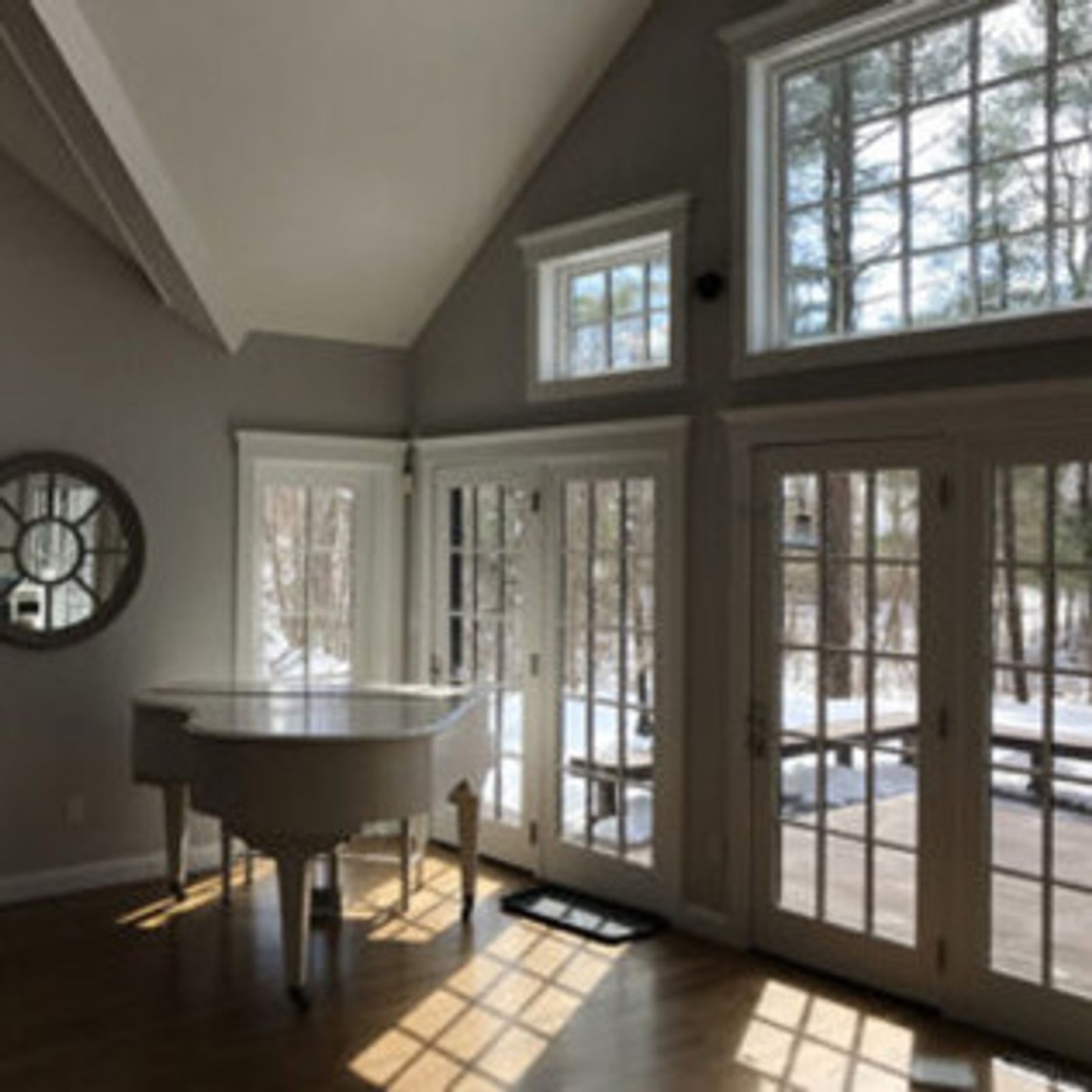White grand piano in a sunlit room with large windows, doors to a snowy deck.
