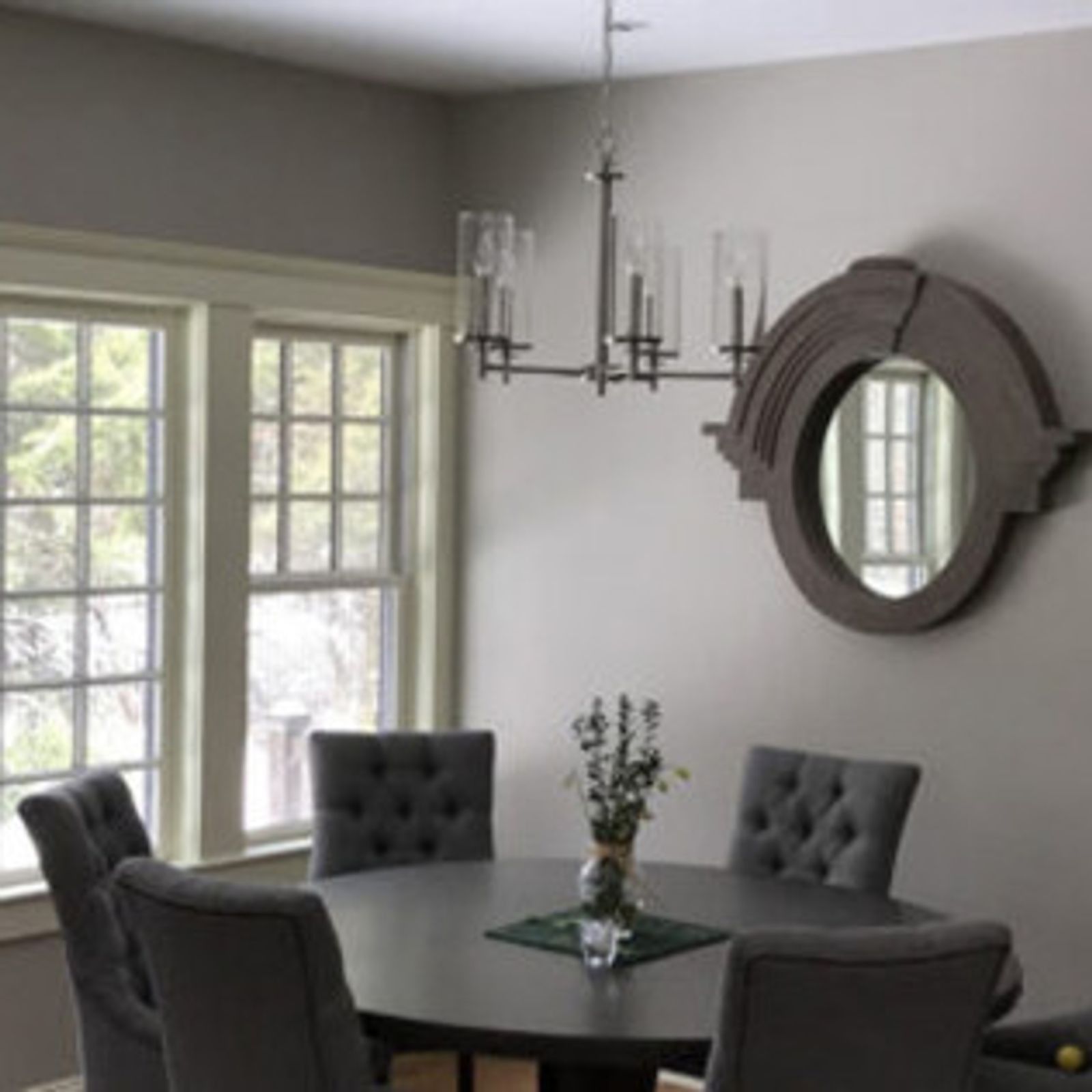 Dining room with round table, gray chairs, chandelier, and a decorative round mirror on the wall.