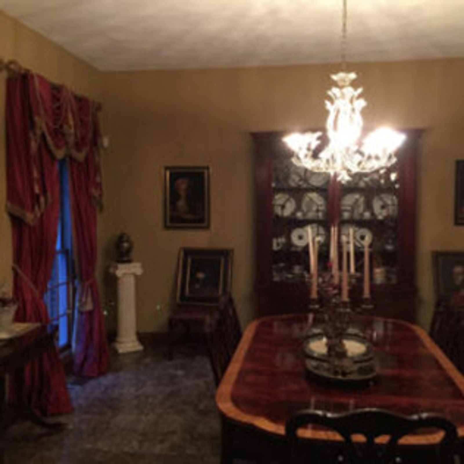 Elegant dining room with red drapes, a chandelier, and a mahogany dining table set for a meal.