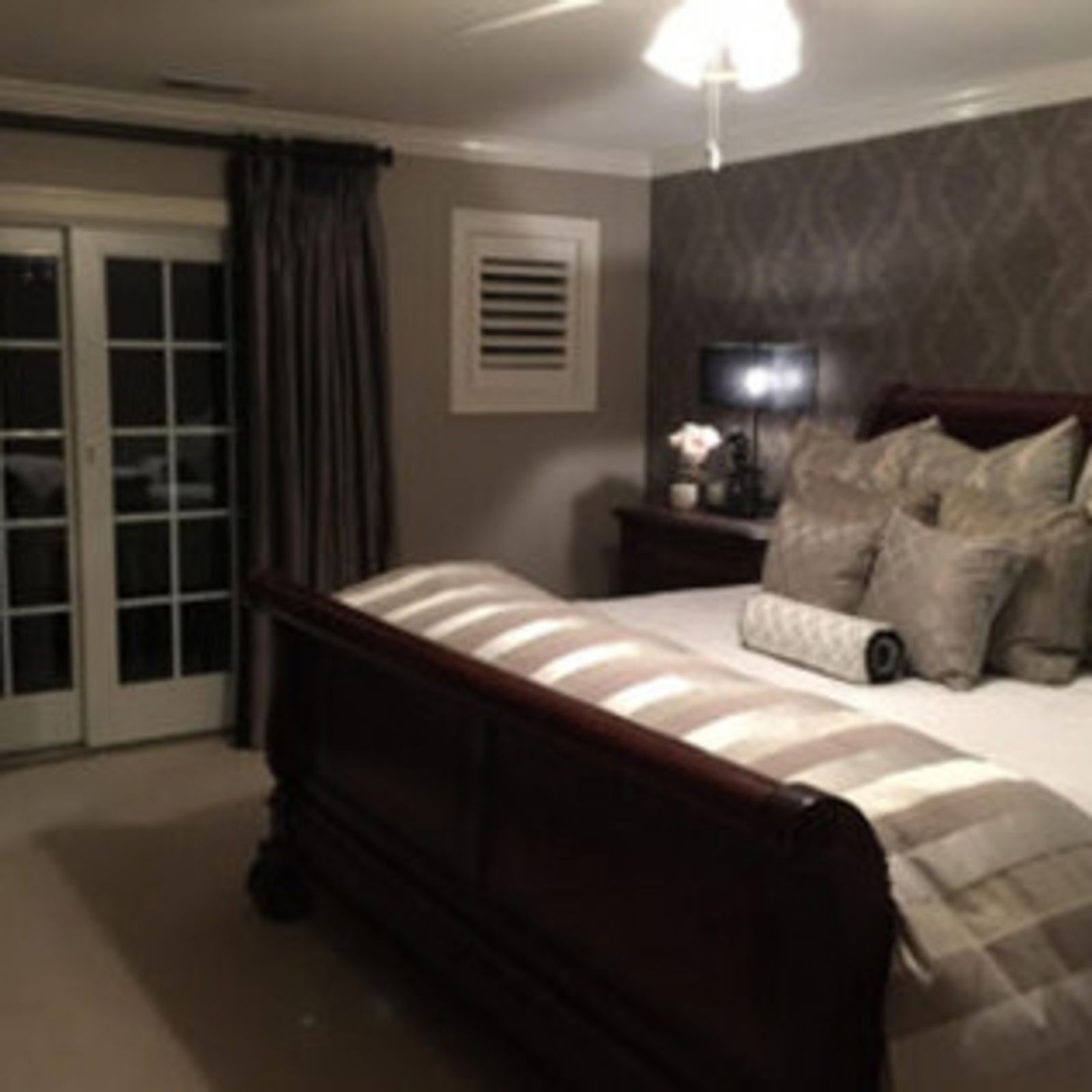 Bedroom with dark wood bed, patterned wallpaper, gray curtains, and glass door.