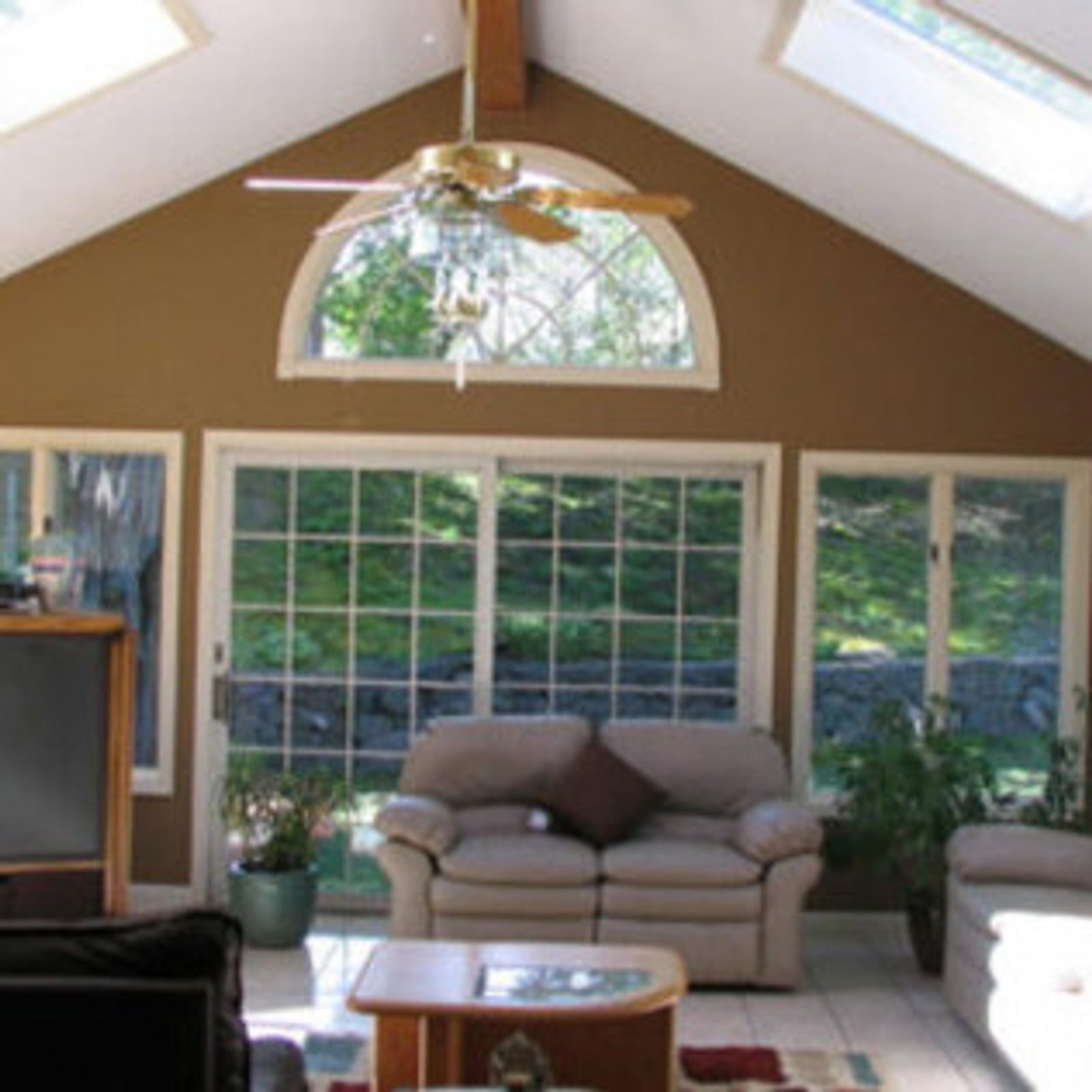 Sunroom with beige sofa, sliding glass doors, arched window, and skylights.