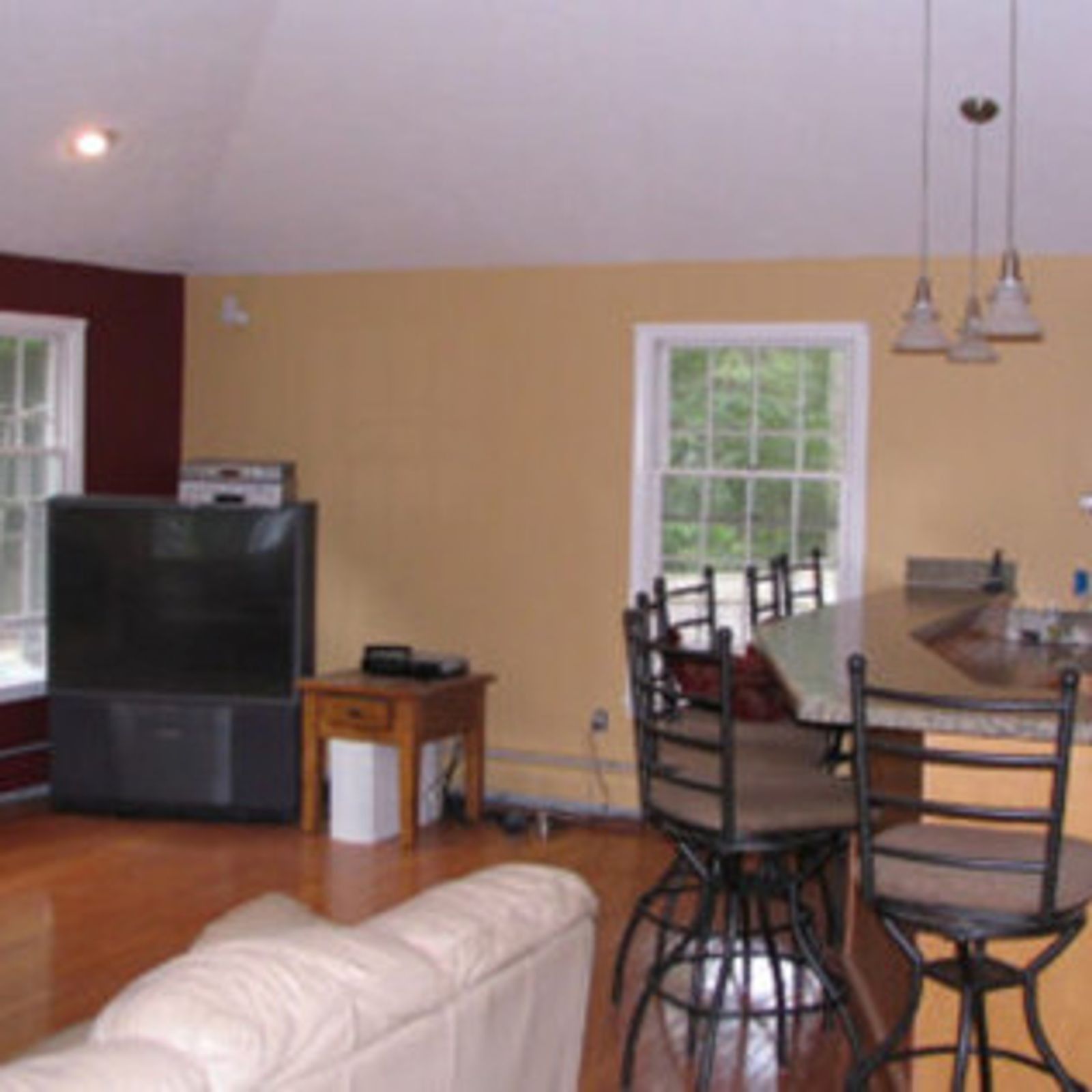 Living room with TV, kitchen counter with stools, and windows; hardwood floors, two tone walls.