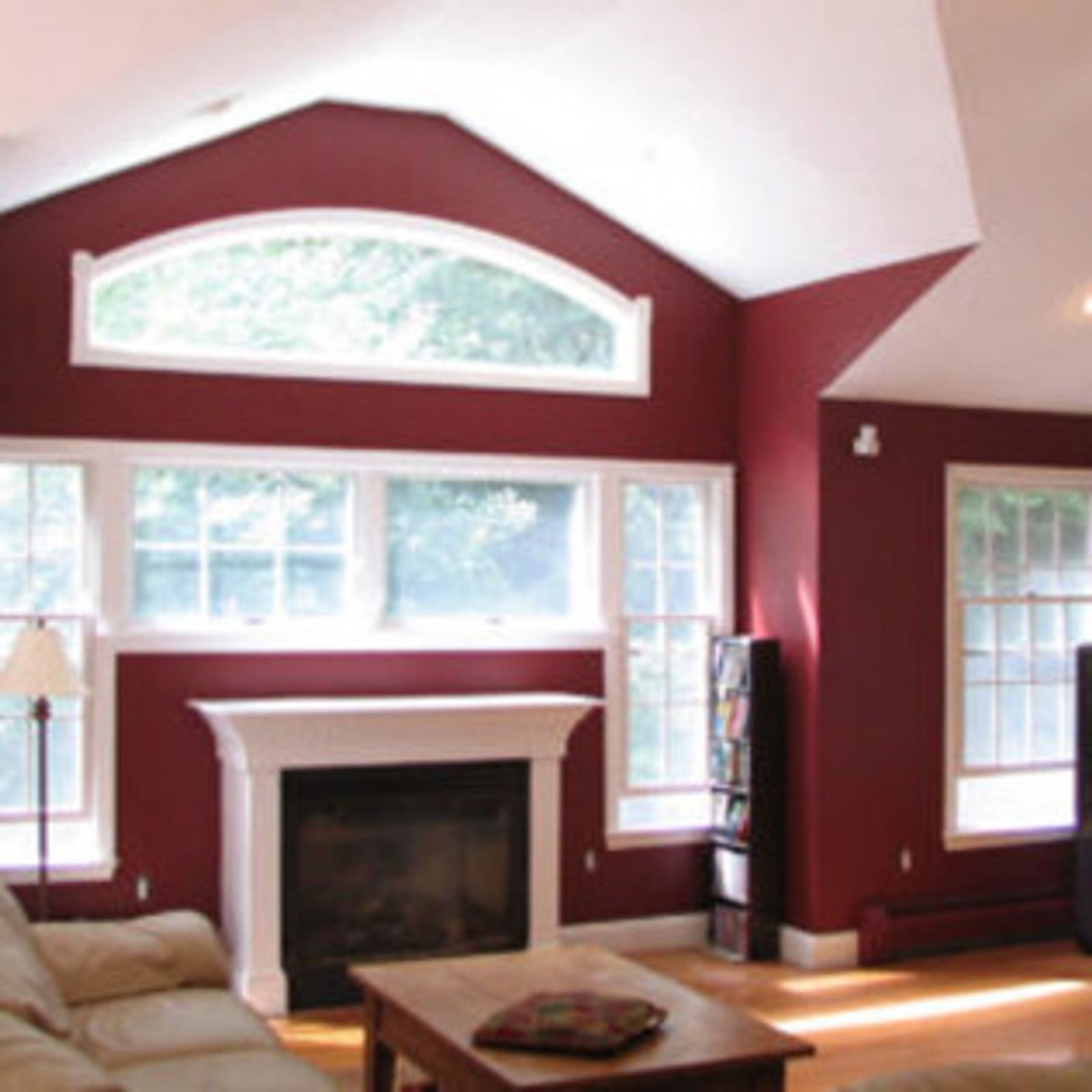 Living room with burgundy walls, white trim, fireplace, windows, and light wood floors.