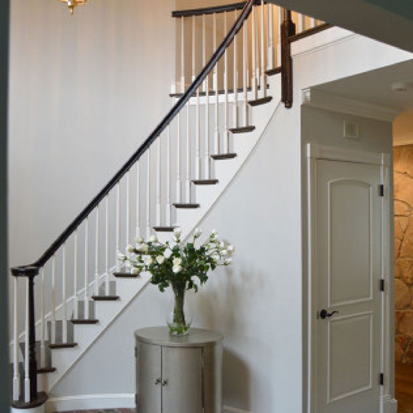 Interior view of a staircase with white balusters, dark handrail, and a small table with flowers.