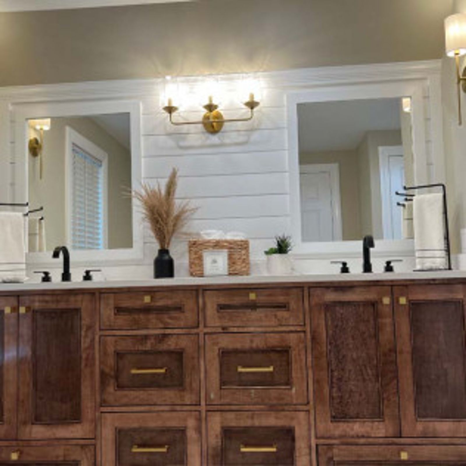 Bathroom vanity with two mirrors, brown cabinets, and gold hardware. White shiplap wall and black fixtures.